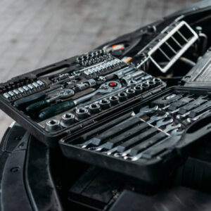 Tool case with wrenches and metal nuts lying on opened car hood in workshop